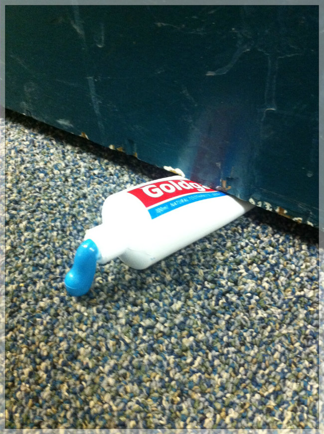 photo of a door stopper that is styled after a toothpaste tube with toothpaste being squished out of it from under the door